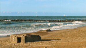 Ein Strand mit brechenden Wellen an einem steinernen Wellenbrecher, einem sandigen Ufer und einem klaren Himmel.