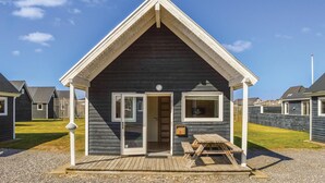 Ein kleines, dunkel gefärbtes Cottage mit Satteldach, einer Holzterrasse und einem Picknicktisch.