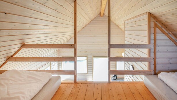 Ein Schlafzimmer im Dachgeschoss mit hohen Decken, Holzbalken, zwei Betten und Blick ins Freie.