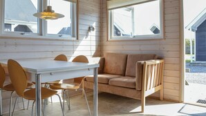 Ein Zimmer mit Holzvertäfelung, einem weißen Tisch mit Stühlen, einer Couch und zwei Fenstern mit Jalousien.