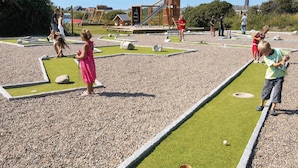 Ein Minigolfplatz mit Puttinggrün, einem Sandbunker und einer Holzkonstruktion im Hintergrund.