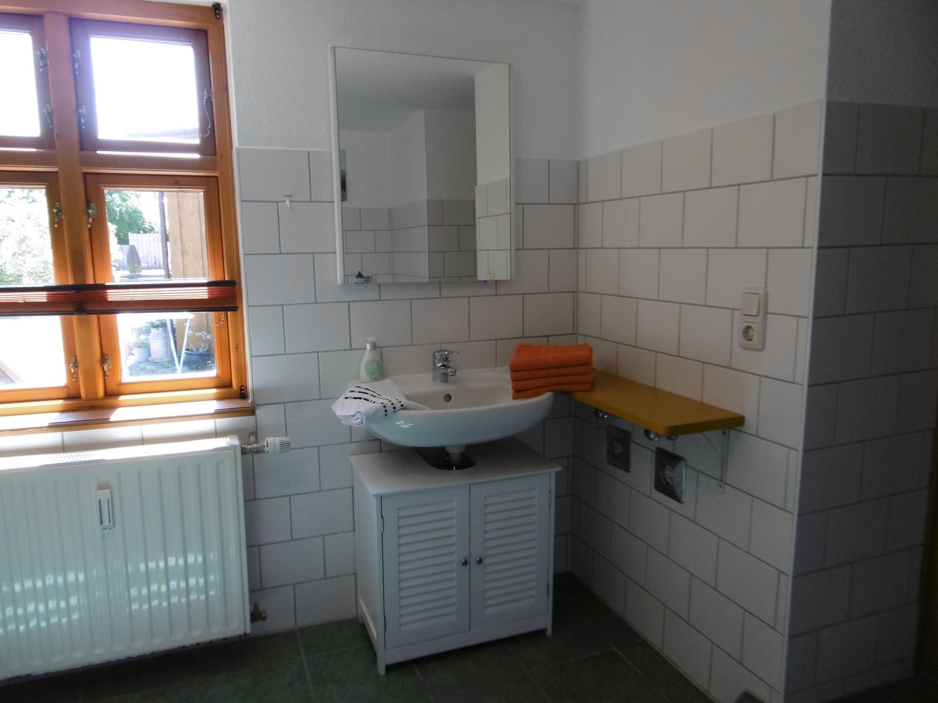 Een badkamer met een wit wastafelmeubel, een spiegel erboven, een raam met houten kozijnen en een radiator.