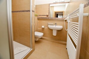 Un baño con ducha, inodoro, lavamanos y perchero para toallas.