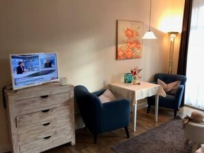 Un salón con televisor, dos sillones, una mesita, una lámpara y un cuadro en la pared.