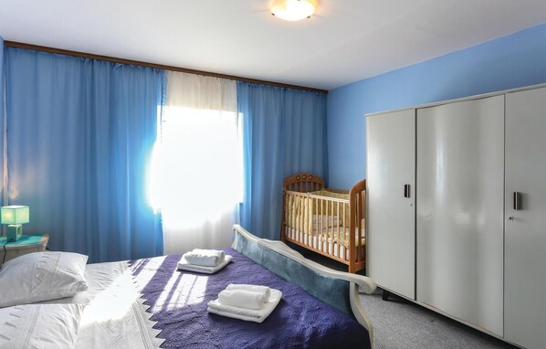 A bedroom with a bed, a crib, a wardrobe, and a window with curtains.