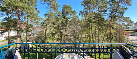 A balcony with a table and chairs, overlooking a forested area and buildings.