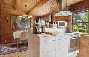 A modern kitchen with wooden walls, a large island, and a view of greenery outside. - Cozy home in Væggerløse with WiFi (Væggerløse)