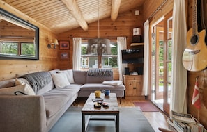 A cozy cabin interior with a wooden ceiling, a sofa, a coffee table, a television, and a guitar. - Cozy home in Væggerløse with WiFi (Væggerløse)