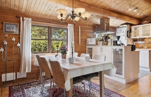 A cozy wooden cabin interior with a dining area, kitchen, and large windows. - Cozy home in Væggerløse with WiFi (Væggerløse)