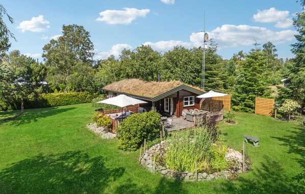 Eine Holzhütte mit einem Reetdach, umgeben von einem gepflegten Garten und einer großen Rasenfläche.