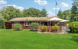 Eine Blockhütte mit einem Reetdach, einem umzäunten Garten und einer Satellitenschüssel.