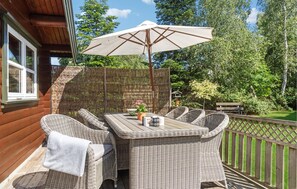 Eine Holzterrasse mit Korbmöbeln, einem Tisch und einem Sonnenschirm.