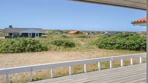 Vista costera desde una terraza de madera que da sobre un área verde con varias casas y un cielo despejado.