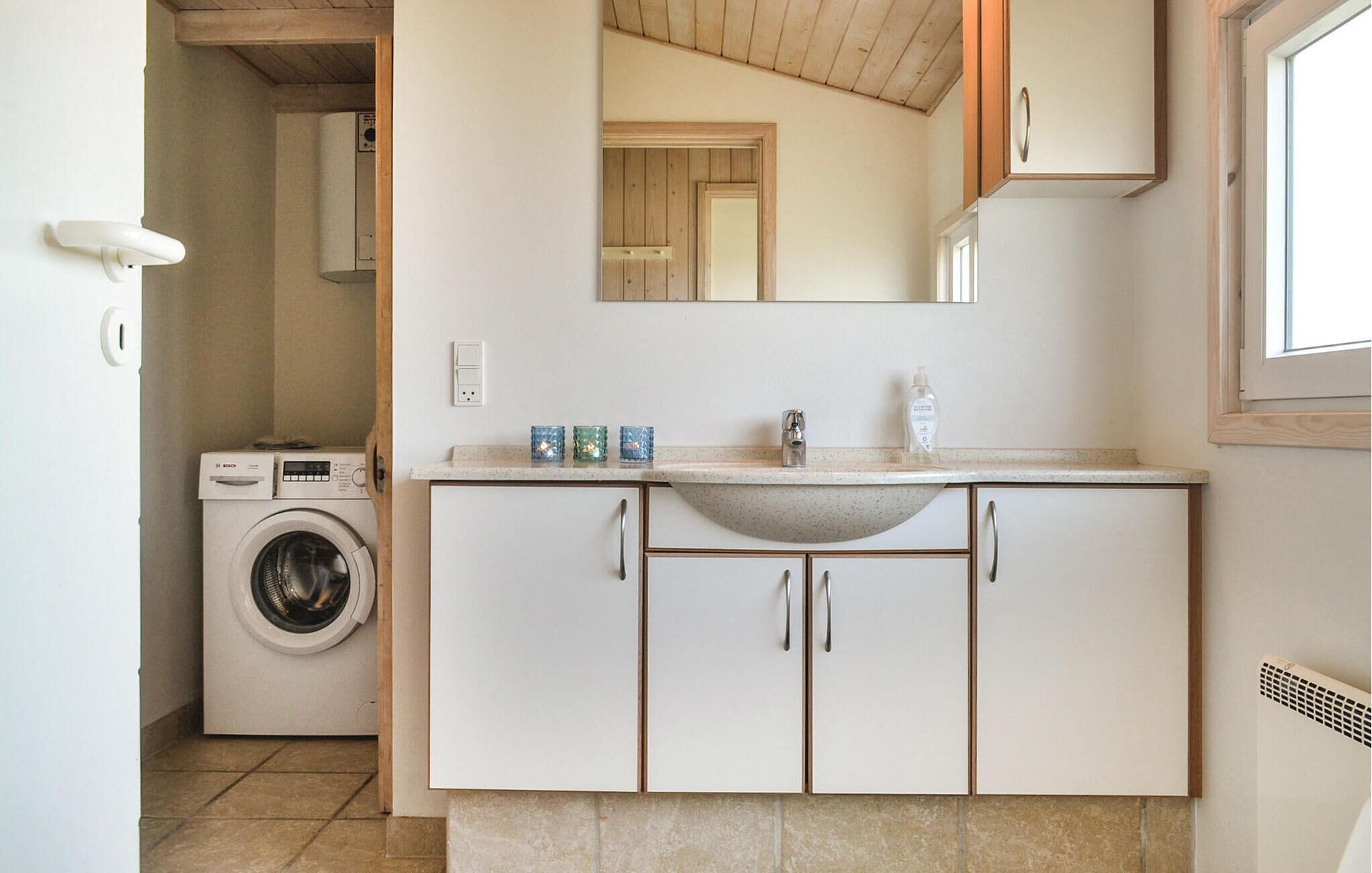 Une cuisine compacte dotée d’un lave-linge encastré, d’un évier avec un plan de travail à motifs et d’armoires en bois.