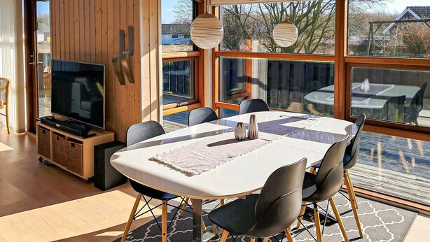 A modern dining area with a white table, black chairs, and a TV on a wooden cabinet. - Gorgeous home in Sydals with sauna (Sydals)