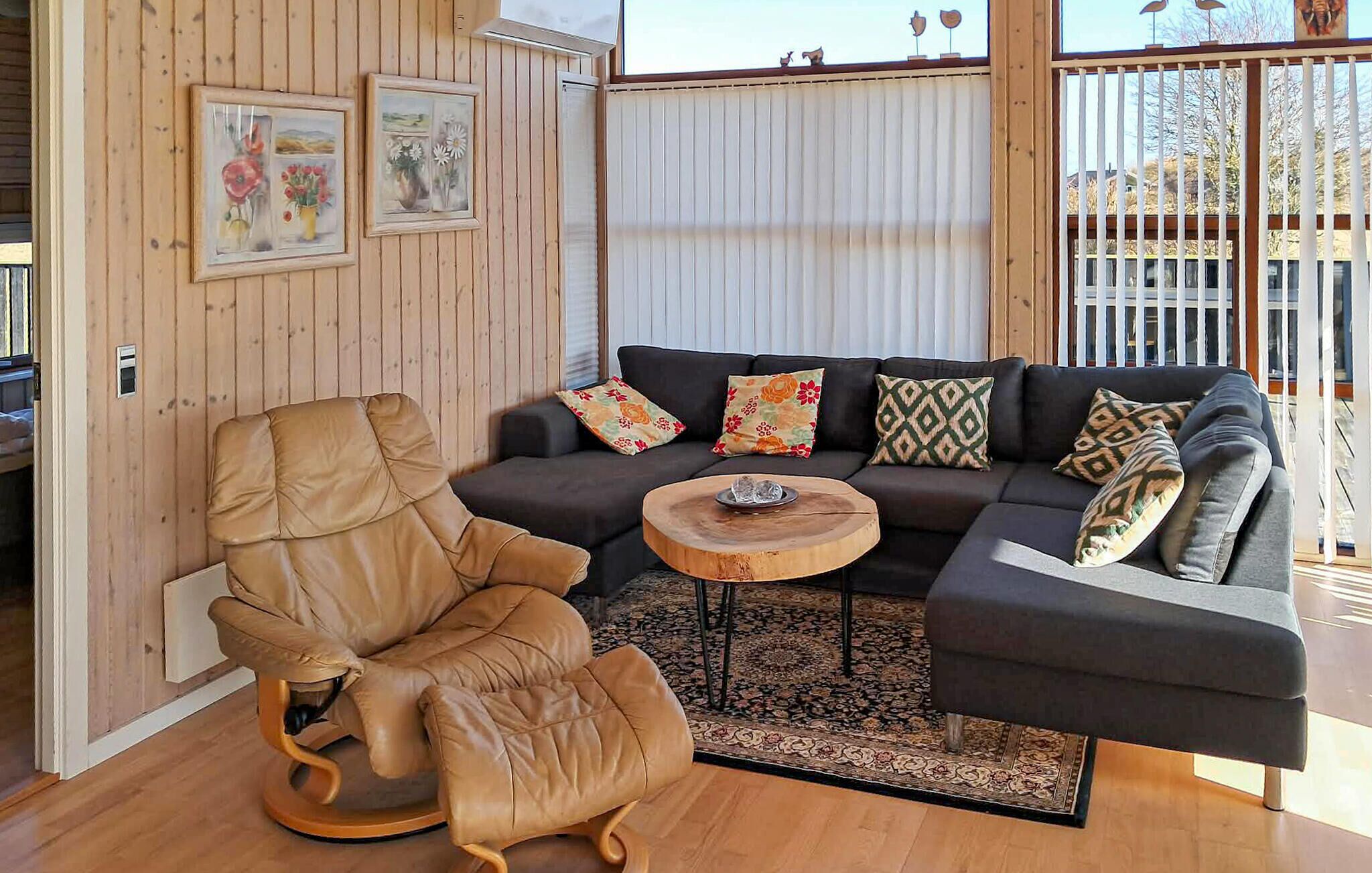 A cozy living room with a brown leather armchair, a dark grey sectional sofa with patterned cushions, and a small wooden coffee table.