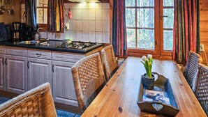 A wooden dining table with wicker chairs, a gas stove, and a window with curtains. - Cozy home in Neede with sauna (Neede)