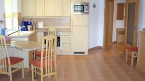 Une cuisine compacte dotée de meubles en bois, d’un four à micro-ondes, d’une machine à café et d’un petit coin repas avec deux chaises.