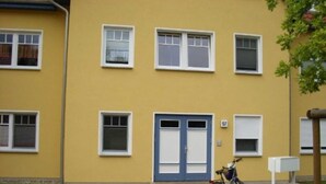 Un bâtiment jaune avec une porte et des fenêtres bleues, un vélo garé devant et une boîte aux lettres.