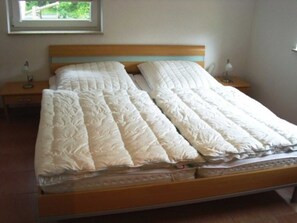 A bed with a wooden frame and a headboard, two bedside tables with lamps, and a window with a view of greenery. - FeWo Furch - * FeWo Furch Chestnuts GM 69256 (Graal-Müritz)
