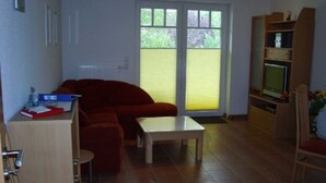 Un espace de vie compact comprenant un canapé, une petite table, un téléviseur posé sur un meuble en bois et une chaise.