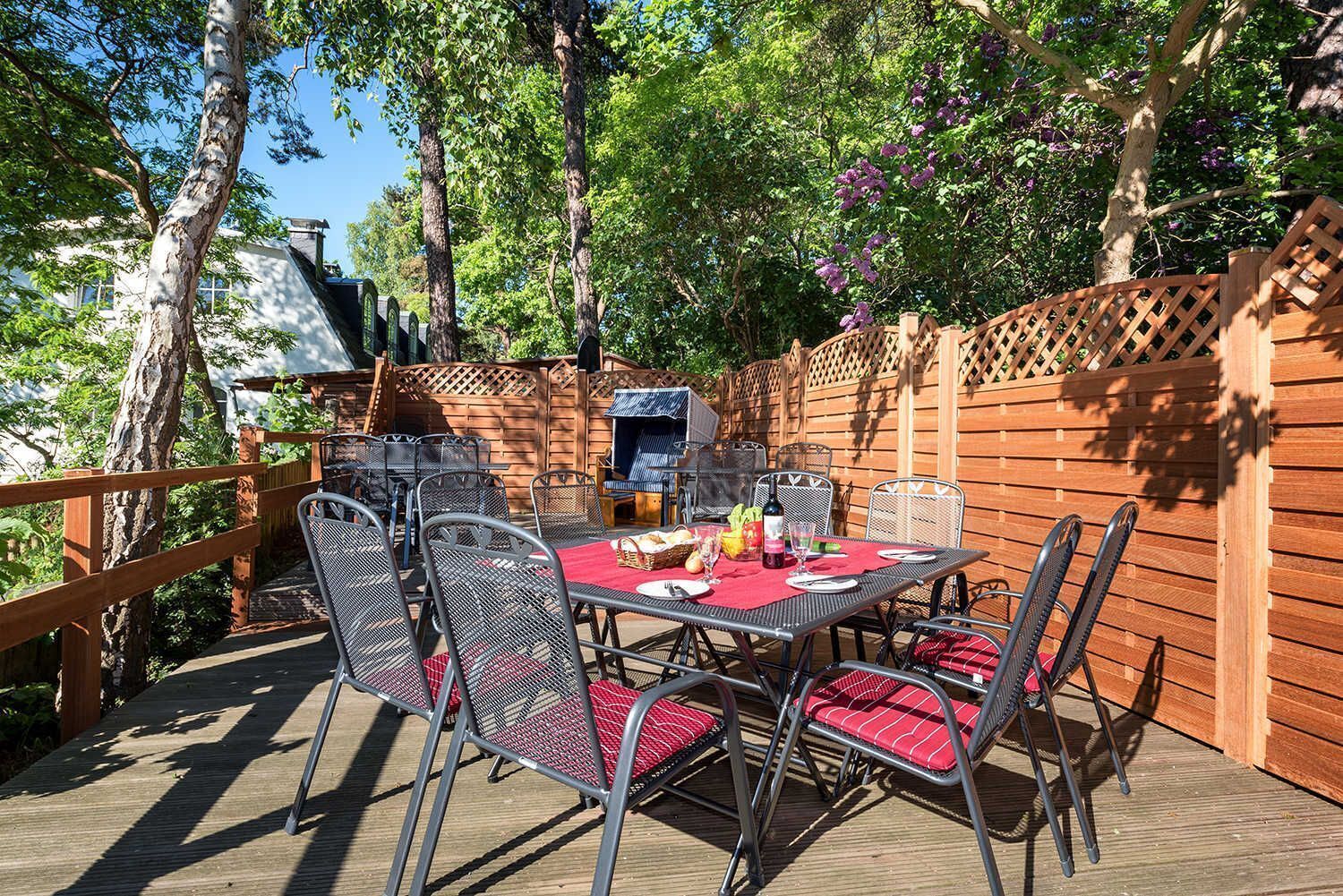 An outdoor patio with a table set for dining, surrounded by metal chairs with red cushions.