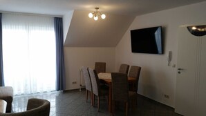 Un comedor con una mesa y sillas, un televisor de pantalla plana montado en la pared y una puerta con teléfono e interfono.