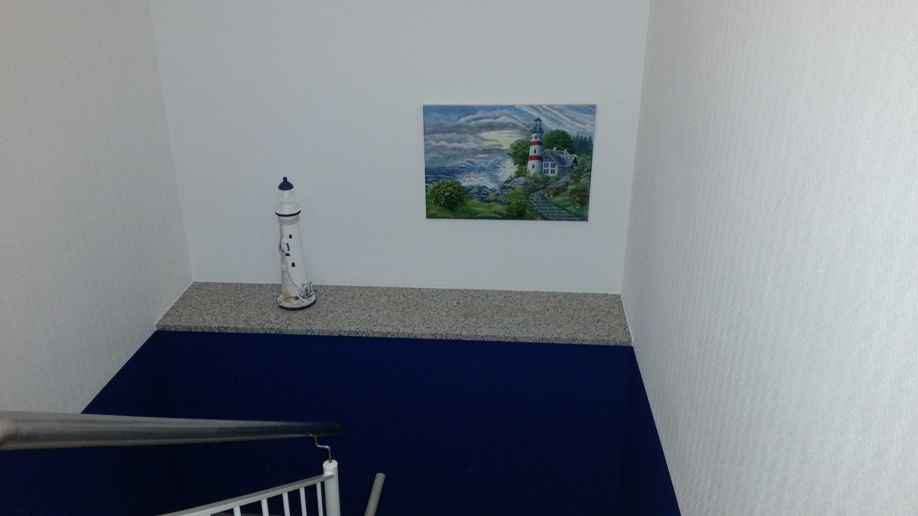 Una escalera con barandilla, una pared blanca y un cuadro de un faro.