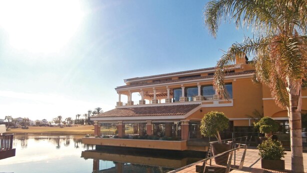 A large, two-story building with a balcony overlooking a body of water, surrounded by palm trees and a clear sky. - 2 bedroom gorgeous apartment in Roldán (Roldán)