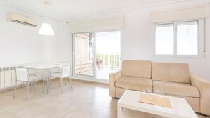 A modern living room with a beige sofa, a white coffee table, and a dining area with a white table and chairs. - 2 bedroom gorgeous apartment in Roldán (Roldán)