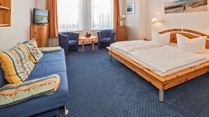 Une chambre d’hôtel comprenant un lit, un canapé, une petite table avec des chaises, une télévision et une fenêtre avec des rideaux.