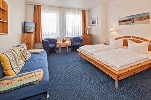 A hotel room with a bed, a sofa, a small table with chairs, a television, and a window with curtains.