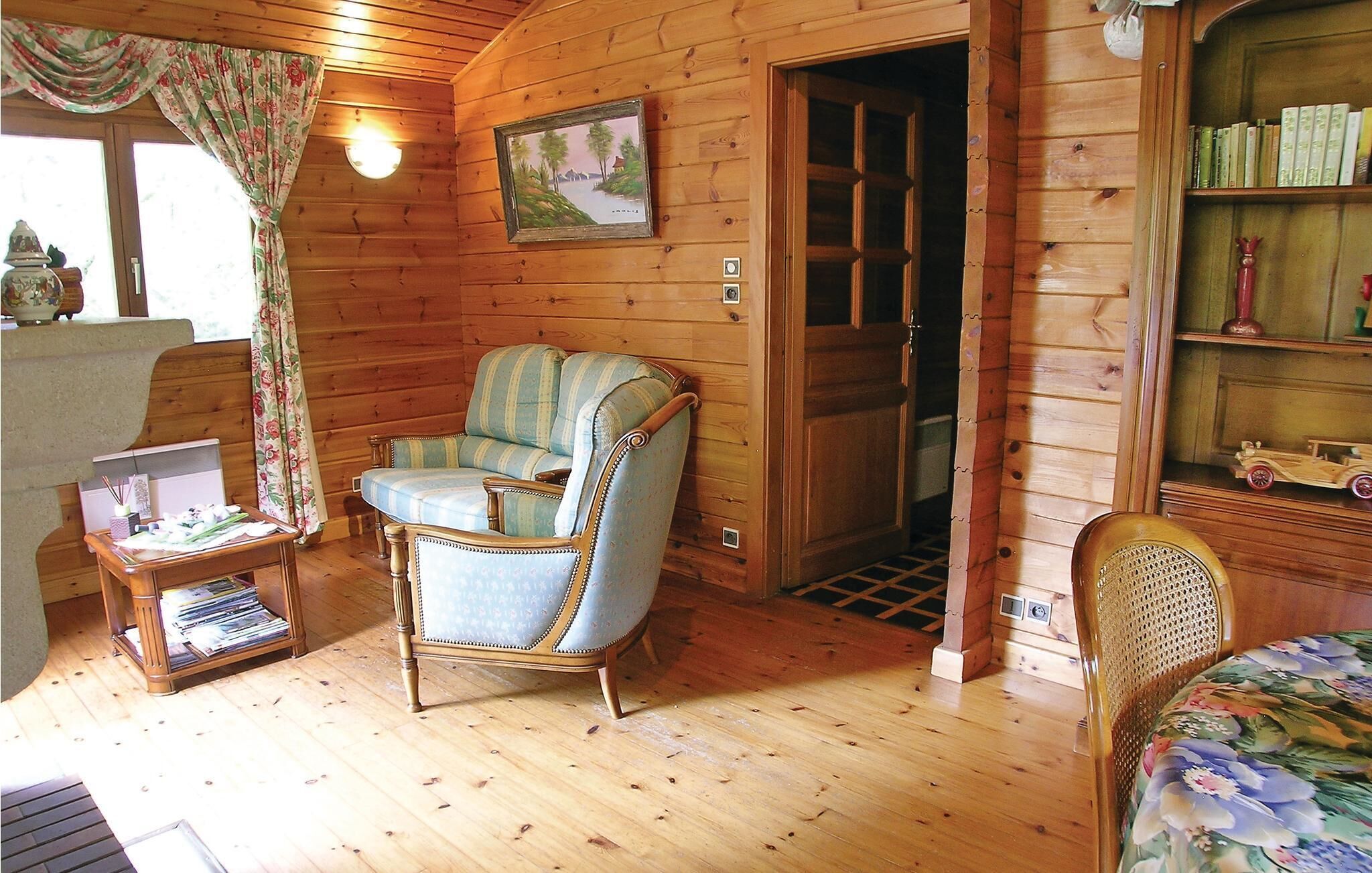 A cozy room with wooden walls, a blue armchair, a wooden bookshelf, and a door leading to another room.
