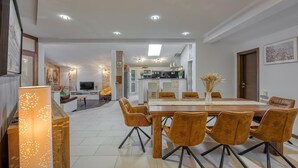 A modern dining area with a wooden table and six chairs, a kitchen in the background, and recessed ceiling lighting. - Cozy apartment in Kanfanar (Kanfanar)