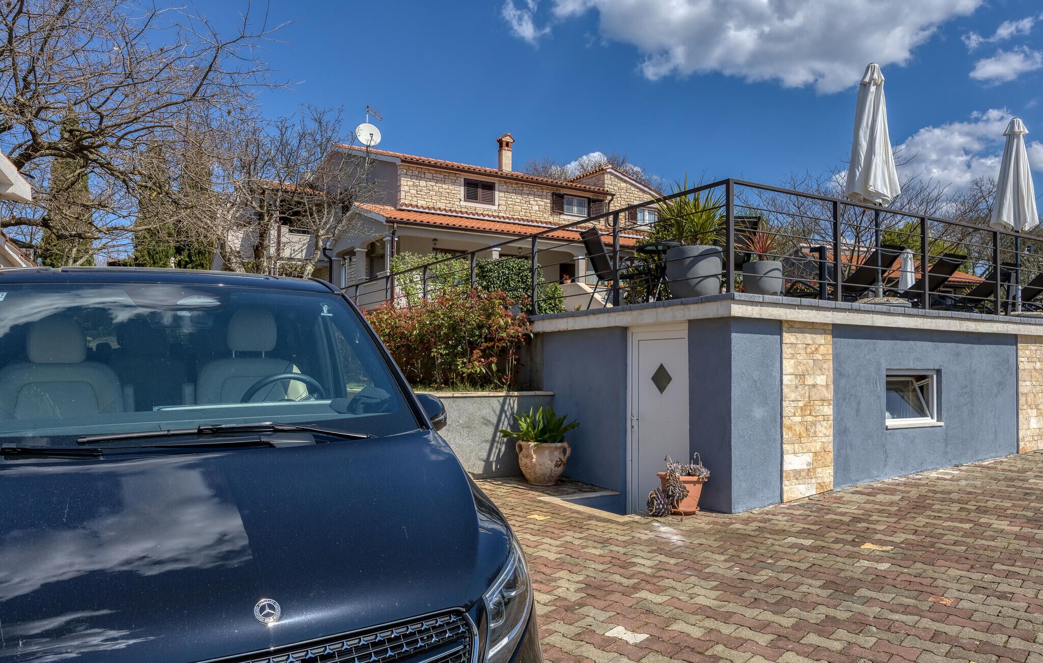 A modern building with a balcony, potted plants, and a car parked in front.