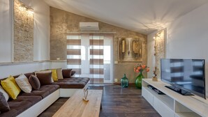 A modern living room with a brown sectional sofa, a wooden coffee table, a flat-screen TV on a white stand, and a large window with striped curtains. - Cozy apartment in Kanfanar (Kanfanar)
