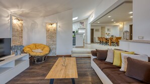 A modern living room with a sofa, a wooden coffee table, and a yellow chair. There is a kitchen area in the background with a dining table and chairs. - Cozy apartment in Kanfanar (Kanfanar)