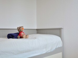 A bed with a white mattress and a brown teddy bear wearing a red shirt.