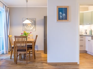 Un comedor con una mesa y sillas de madera, un reloj en la pared y una cocina al fondo.