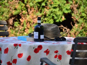 A bottle of wine, a woven hat, and a book on a table with a floral tablecloth.