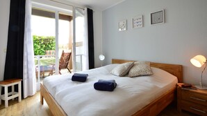 A bedroom with a large bed, a wooden nightstand, a desk, and a chair. There is a sliding glass door leading to an outdoor area. - Wohnpark An der Muehle Whg Cuba1-1 .. - Cuba 1. 1 (Kühlungsborn)