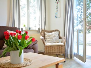 A living room with a brown sofa, a wicker chair, a wooden table, and a vase of red tulips.