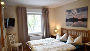 A bedroom with a bed, a chair, a TV, a window with curtains, a lamp, and a painting on the wall. - Apartment 1 - Usedom Landhaus Morgenitz (Mellenthin OT Morgenitz)