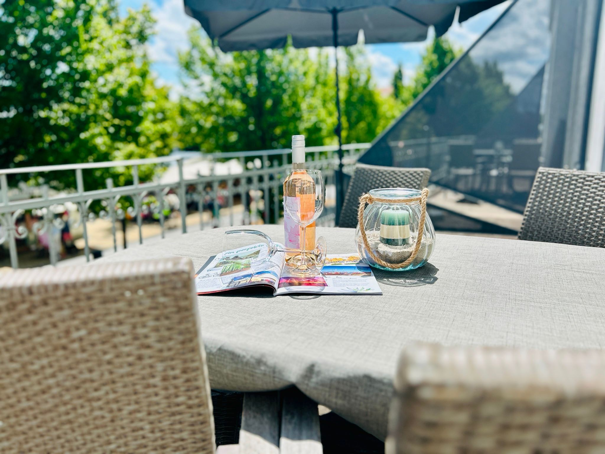 Een terras met rieten meubels, een kandelaar van glas en een tijdschrift op de tafel.