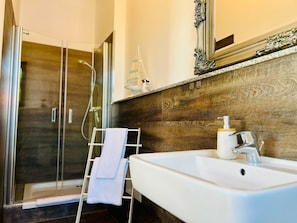 A bathroom with a shower, a white sink, a towel rack, and a decorative mirror.