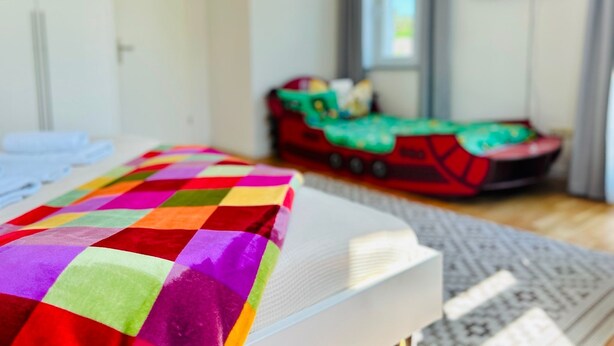 A bed with a colorful quilt, a small red toy train, and a television on the wall.
