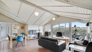 A spacious living area with a high ceiling, a fireplace, a television, and a large window offering a view of the outdoors.