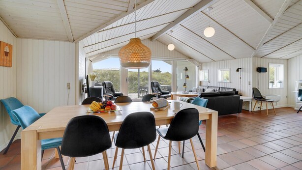 A spacious dining area with a long wooden table, black chairs, and a hanging light fixture.