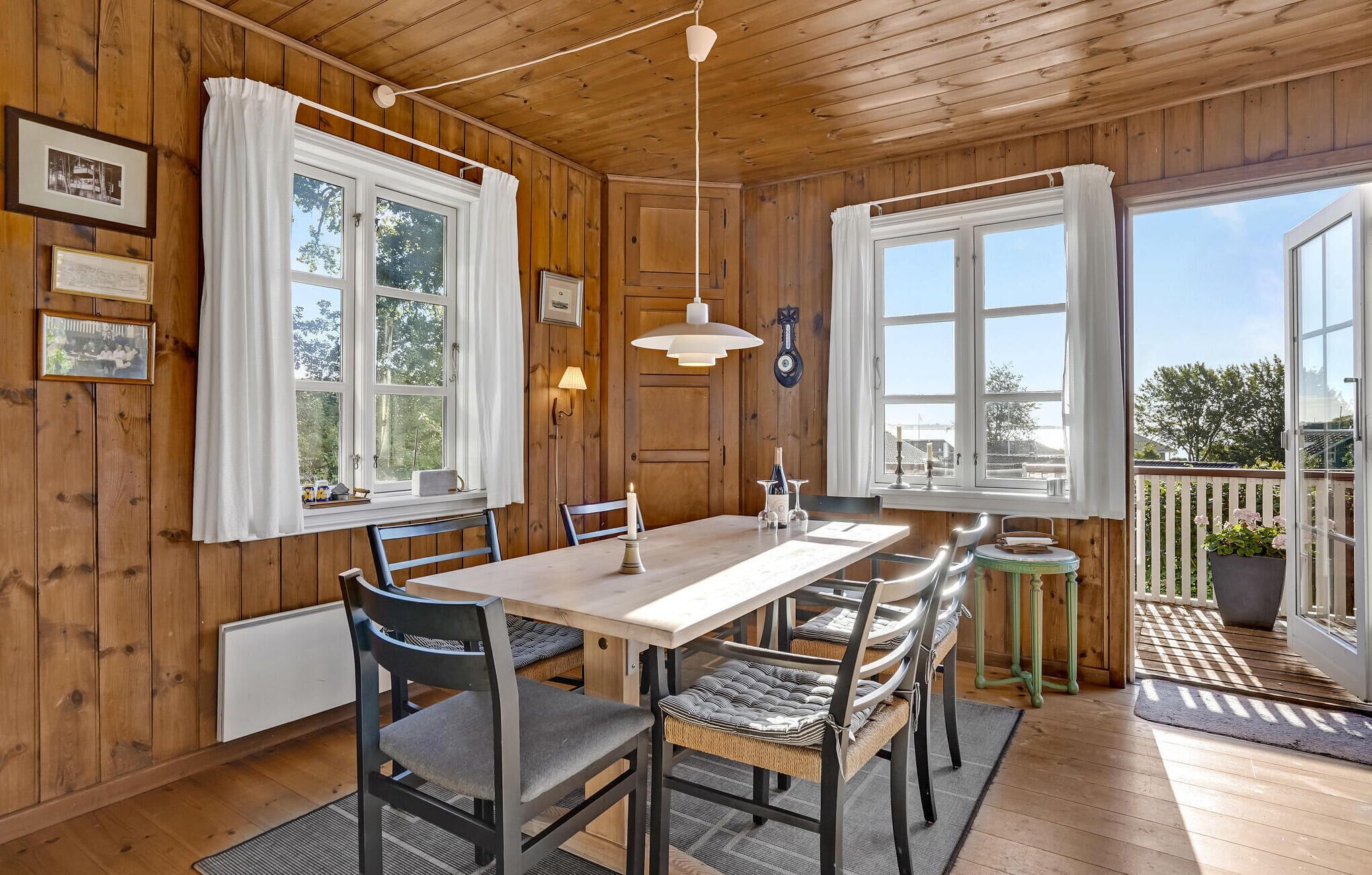 A wooden cabin with a dining area featuring a table, chairs, and a hanging light fixture.