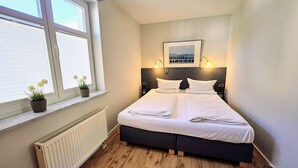 Een slaapkamer met een bed, een radiator, een raam met zonwering, een kamerplant en een fotolijst aan de muur.